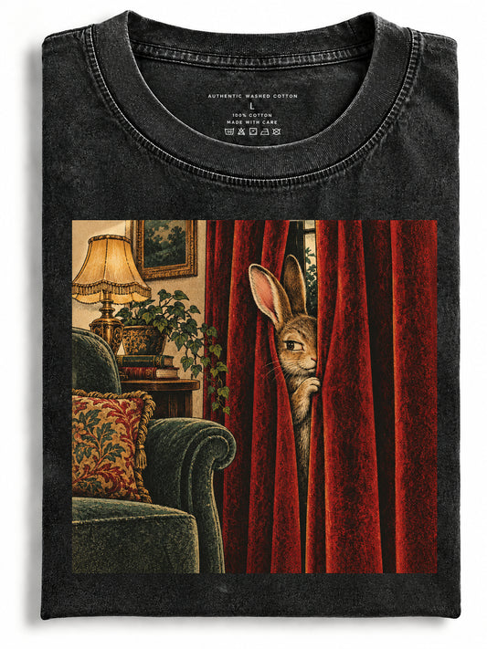 Folded black washed t-shirt featuring artwork of a rabbit peeking behind red curtains